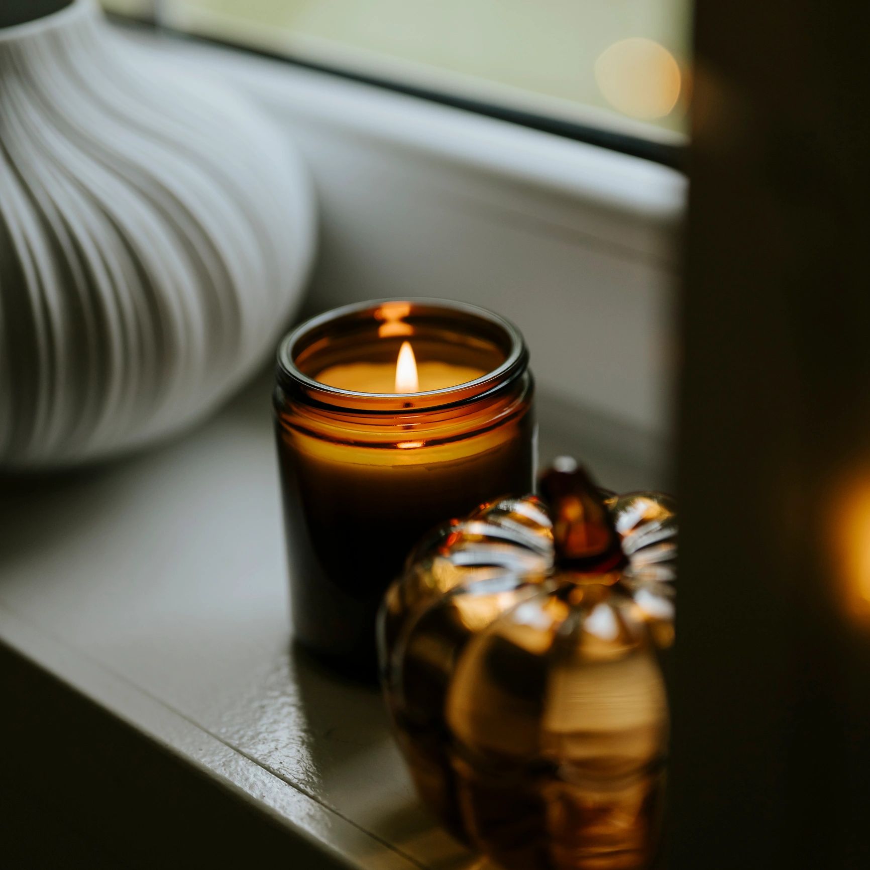 Autumn decor still life with glass pumpkin and scented candle on a window sill